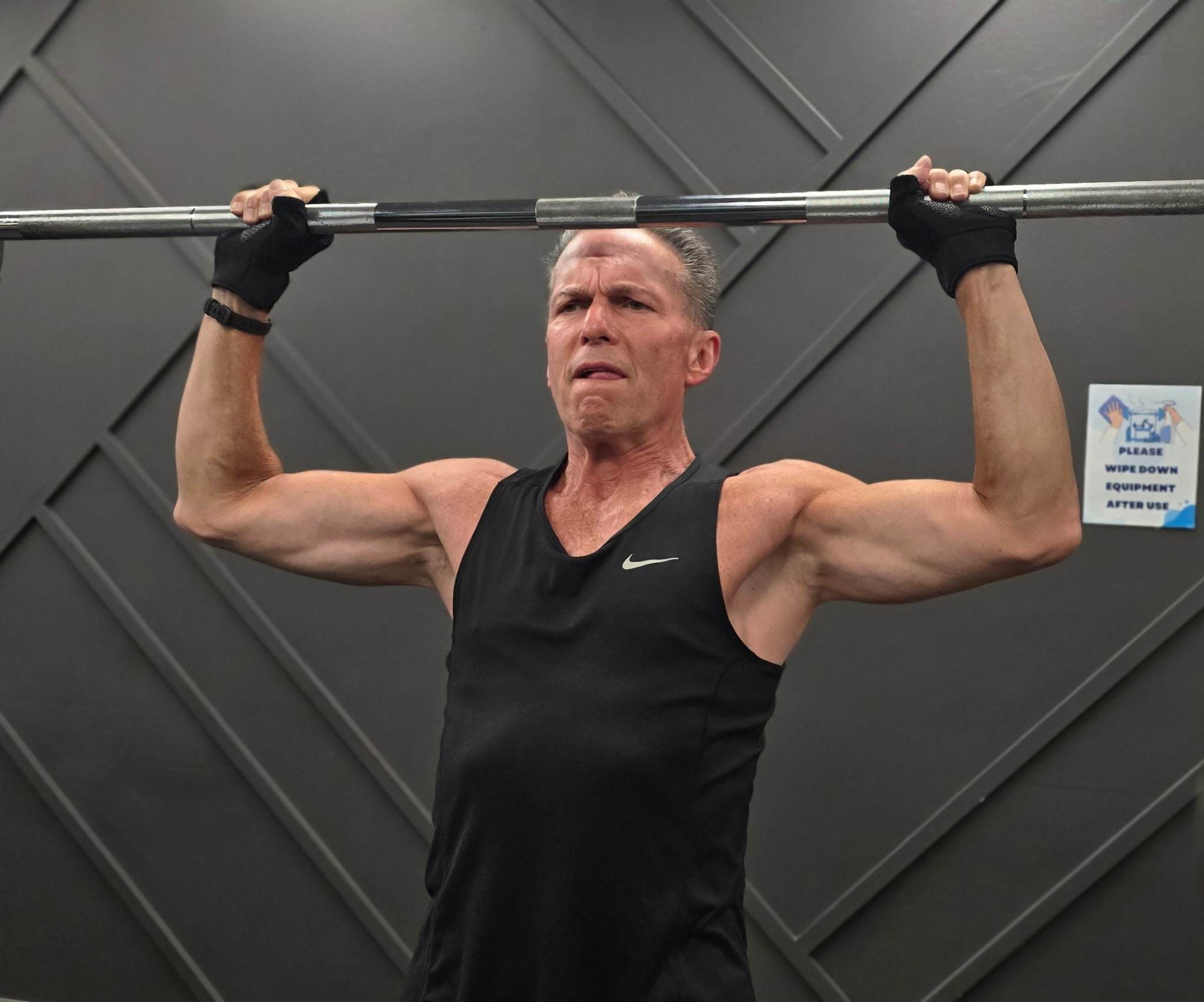 A member over 50 gripping a barbell overhead at Balanced Health Fitness in Seaford, NY.